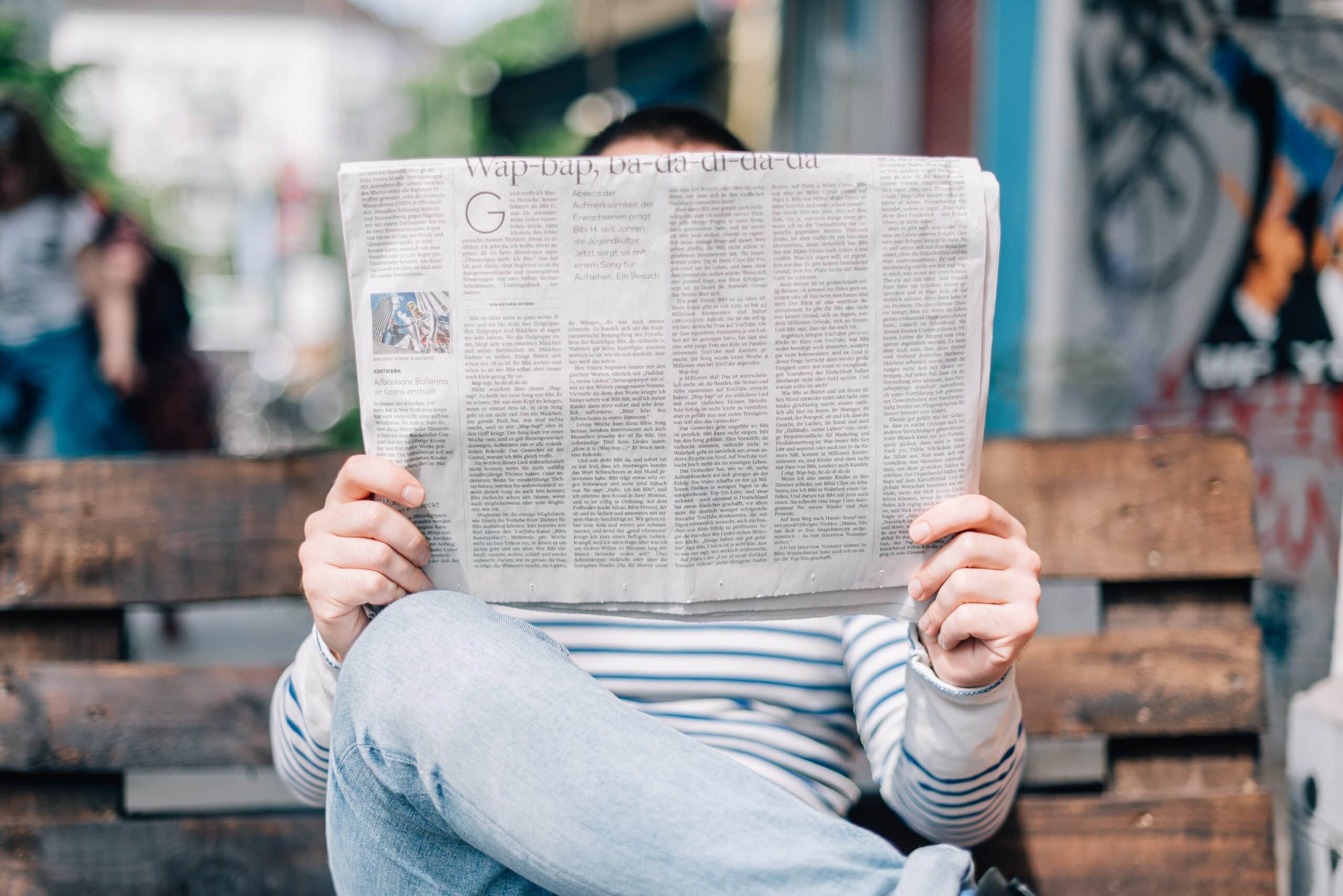 a gentleman reading a newspaper on a bench in city centre